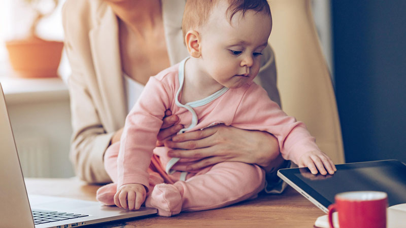 εργαζόμενη μητέρα με το μωρό μπροστά από το λάπτοπ της