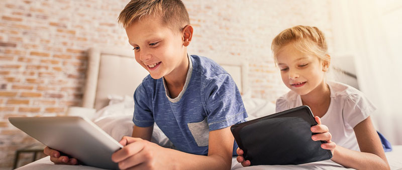 παιδιά ξαπλωμένα στο κρεββάτι παίζουν στα tablet τους