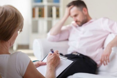 θεραπεύτρια σε συνεδρία με θεραπευόμενο που πιάνει το κεφάλι του
