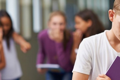 αγόρι με λευκή μπλούζα στέκεται στεναχωρημένο ενώ πίσω τα άλλα παιδιά του ασκούν bullying