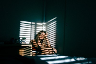 γυναίκα στο κρεββάτι που τη χτυπάει ο ήλιος μέσα από περσίδες