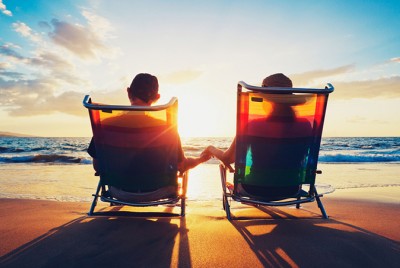 ζευγάρι καθισμένο σε ξαπλώστρες κοιτάζει το ηλιοβασίλεμα