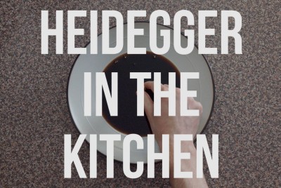ένα χέρι πάνω από ένα πιάτο και μία επιγραφή heidegger in the kitchen