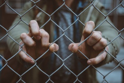χέρια ενός άνδρα που κρατούν σφιχτά ένα συρματόπλεγμα
