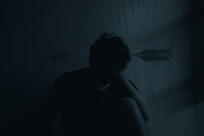άνδρας καθισμένος στο πάτωμα με την πλάτη σε τοίχο ζωγραφισμενο με βροχή αναγνωρίζει την επίδραση της αρνητικής σκέψης στον εγκέφαλό