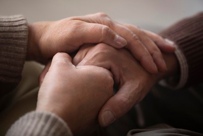 χέρι που κρατάει το χέρι μίας ηλικιωμένης και της δείχνει το ανθισμένο  λουλούδι 