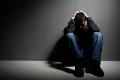 άνδρας που κάθεται σε σκοτεινό τοίχο και πιάνει το κεφάλι του
