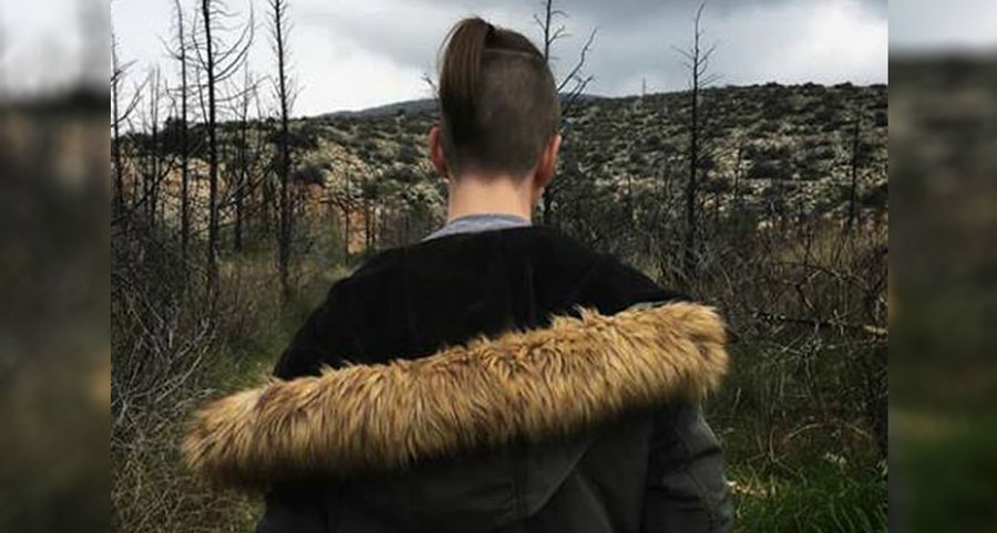 έφηβος με κοτσιδάκι και μπουφάν που βρίσκεται σε δάσος με γυρισμένη την πλάτη στην φωτογραφική κάμερα