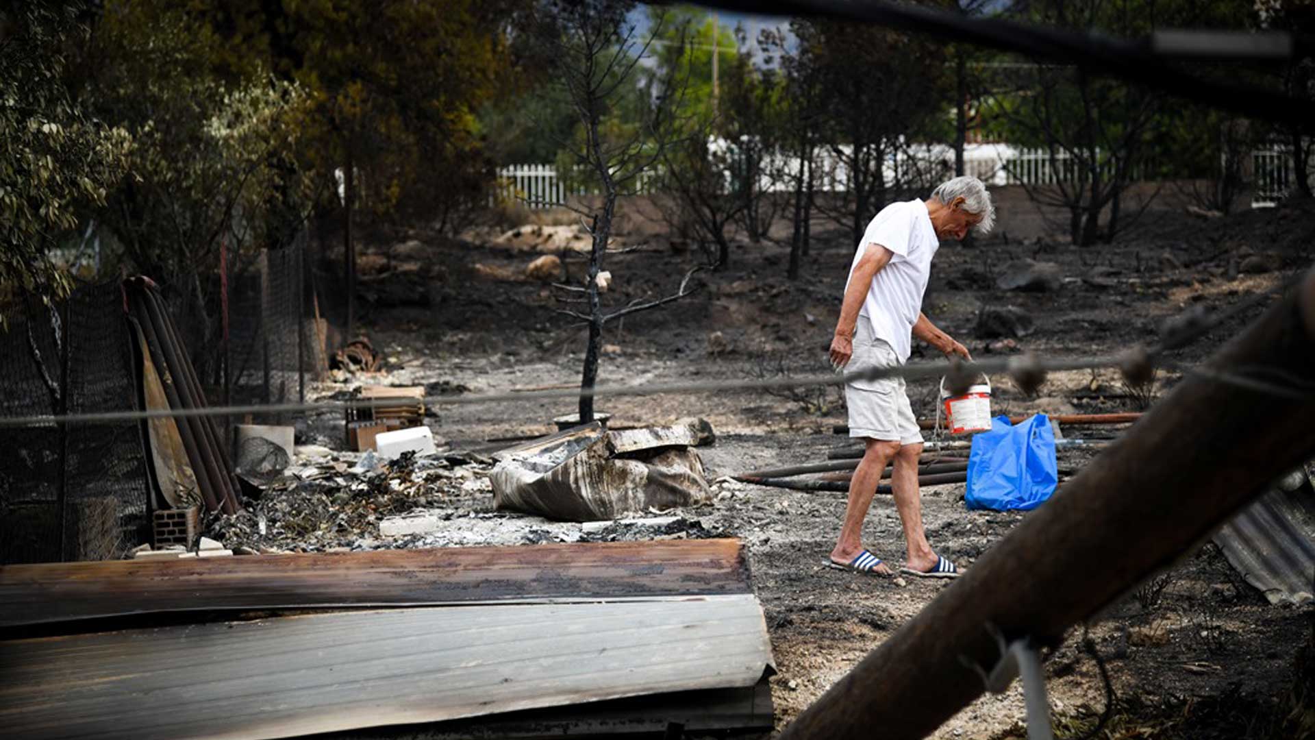 άνθρωπος κρατάει ένα κουβά μέσα σε καμμένο τοπίο